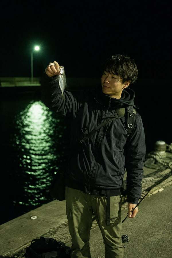 夜の漁港で常夜灯の下、釣り上げたアジを掲げる男性
